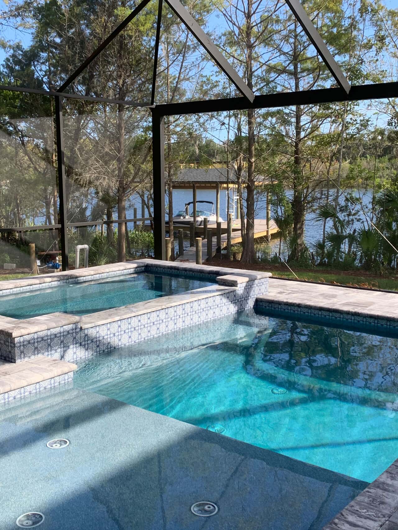 Photo of a pool with hot tub inside of. screenroom with water in the background